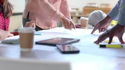 Midsection of diverse architects discussing blueprints on table in office, slow motion