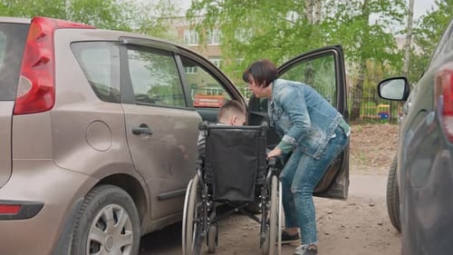 Woman Helps Child in Wheelchair get into Car