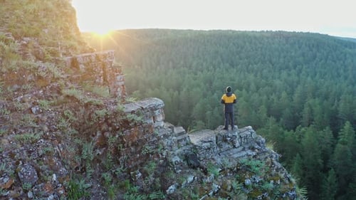 Flying Around Young Man Standing on the Edge of High Rocky Cliff