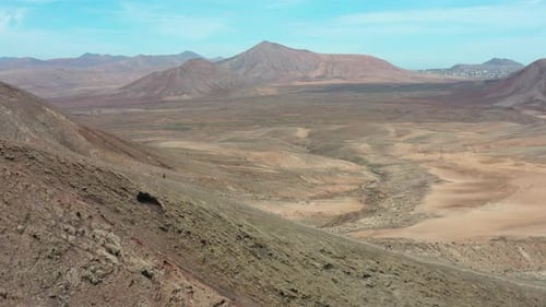 Aerial View of Female Hiker Descending Red Mountain Ridge in Fuerteventura Desert Landscape