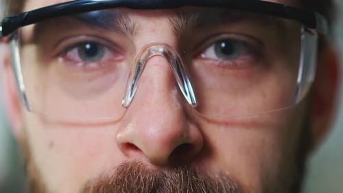Close Up of Serious Face of Caucasian Male Workman of Factory in Goggles Standing at Production Site