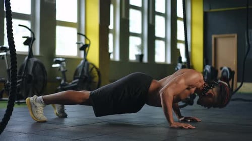 A Young Mixed Race Man with Dreadlocks and Athletic Shorts Doing Pushups in a Modern Gym