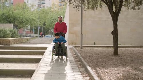 Father Pushing the Wheelchair of His Son with Tetraplegia During a Walk Together Outdoors