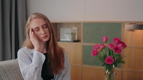 Young Woman in Her Apartment Rubbing Her Temples Visibly Exhausted and in Pain From a Tension
