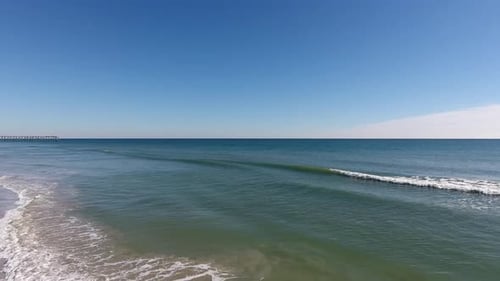 Drone shot flying away from the gentle ocean waves towards the beach. A family watches the ocean tid