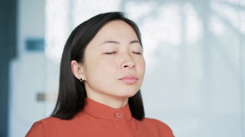 Close up of asian woman relaxing with her eyes closed in a modern office. Portrait of a calm happy