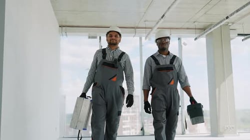 Trabajadores de la construcción indios y africanos en uniforme y cascos caminando con herramientas en la construcción
