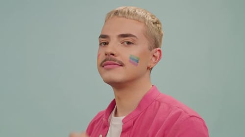 Gay Man with Rainbow Flag on Cheeks Wearing Pink Shirt Smiling at Camera