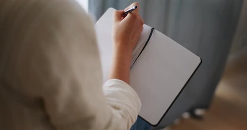 Person Writing in Notebook with Pen Indoors