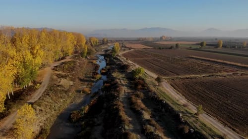 Autumn colors on countryside landscape with yellow trees and brown lands alongside river