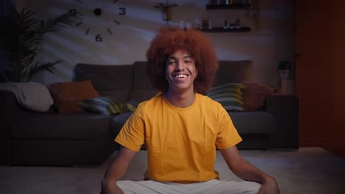 Smiling Man Sits Cross Legged on Rug Indoors