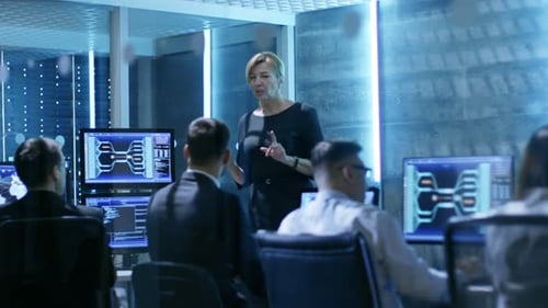 Una supervisora dirige una sesión informativa para sus empleados en la Agencia de Vigilancia del Gobierno. La habitación es divertida