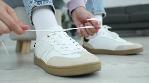 Woman tying shoelace of white sneaker indoors, closeup
