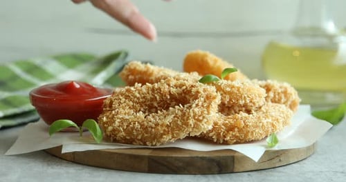 Woman taking tasty deep fried squid ring and dipping it into ketchup at grey textured table, closeup