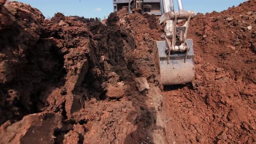 Excavator Digging a Trench in Red Soil