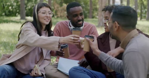 Diverse Group of Friends Students Clinking Coffee Cups and Eating Sanwiches Enjoying Picnic in Park