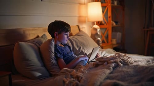 Petit garçon utilisant une tablette au coucher, couché à la maison, lit, gros plan, contenu de navigation pour enfants