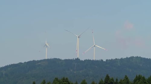 Wind Turbines Spinning Atop Tree-Covered Hill