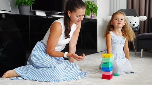 Kleines Mädchen mit ihrer Mutter spielt zu Hause ein Jenga-Brettspiel und nimmt bunte Holzblöcke