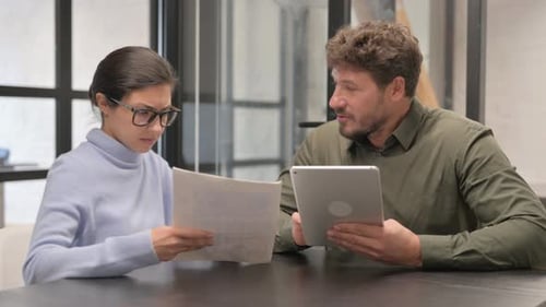 Teamkollegen erledigen Papierkram mit digitalem Tablet und diskutieren