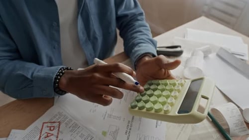 Black Man Using Calculator to Manage Finances at Messy Table with Overdue Bills