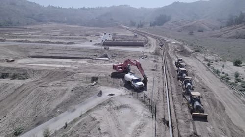 A drone circles above heavy construction parked outside a home construction site, poised and ready t