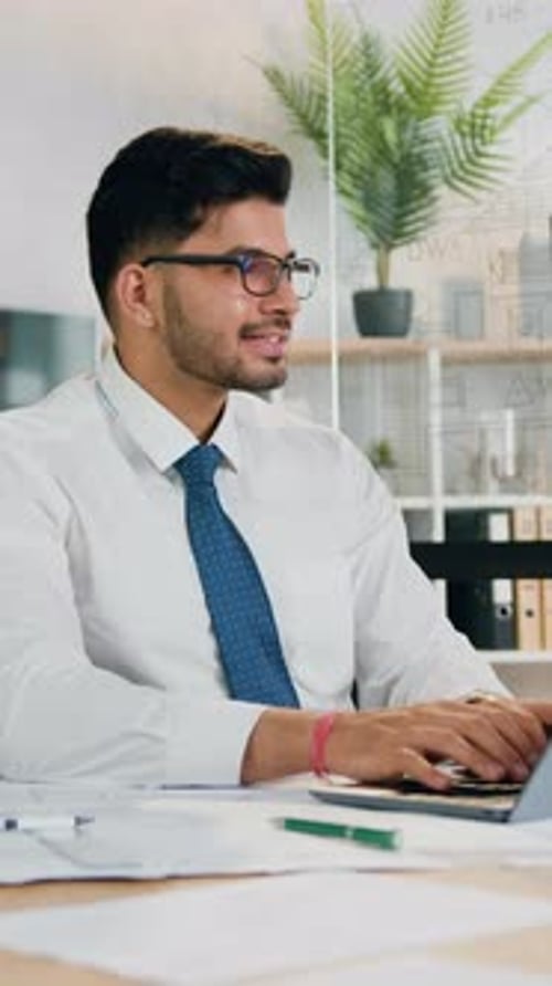 Flux de travail au bureau où un bel homme barbu qualifié, positif et performant, portant des lunettes, travaille