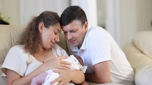 Couple Holding Newborn Infant on Couch at Home