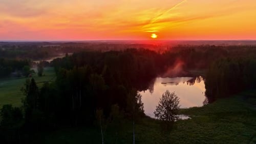 Sunset over small forest lake with soft orange glow and rising mist