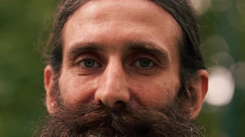 portrait of smiling adult man with gray beard and long hair in park close-up of eyes