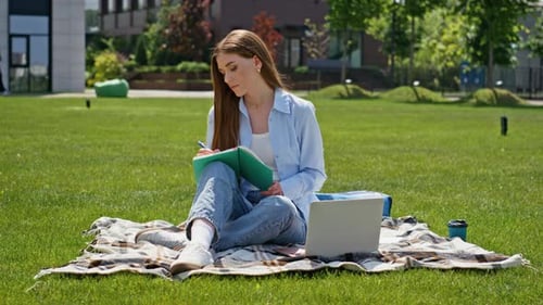 Junge Frau studiert Rasen auf dem Campus, schreibt im Notizbuch und konzentriert sich auf studentisches Lernen