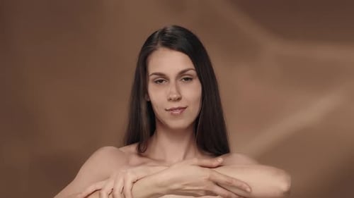 A Seminude Woman Enjoys the Velvety and Softness of the Skin of Her Hands in the Studio on a Brown