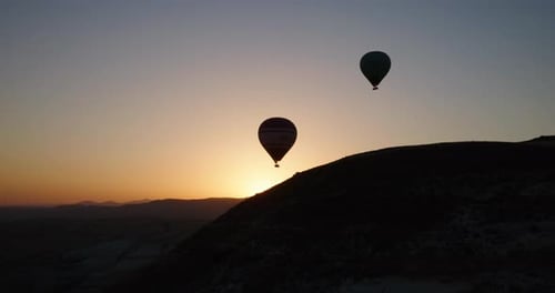 Two hot air balloons flying over a hill in Cappadocia, Turkey, at sunrise