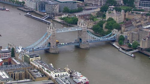 Aerial rotating shot of Tower Bridge with cars traveling along with a warship in the Thames