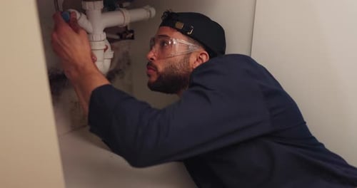 Man Repairing Sink Plumbing with Safety Glasses
