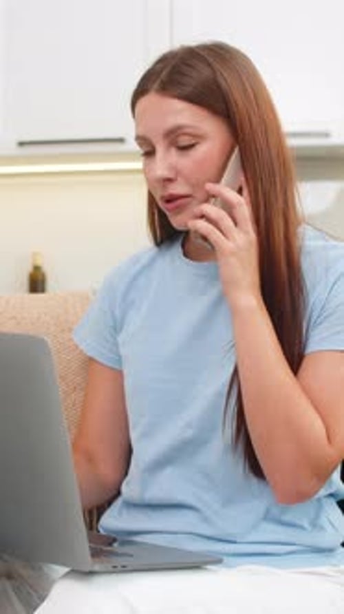 Young Woman Works on Laptop and Talks on Smartphone Multitasks with Focus Handles Tasks and Client