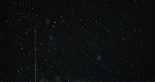 Winter snowfall at night snowing on city street in street light. Snow flakes falling in slow motion