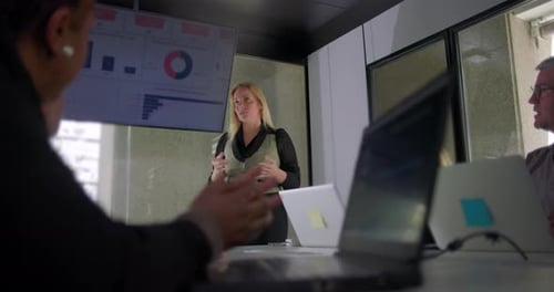 Businesswoman explaining data during meeting as team listens attentively in modern office