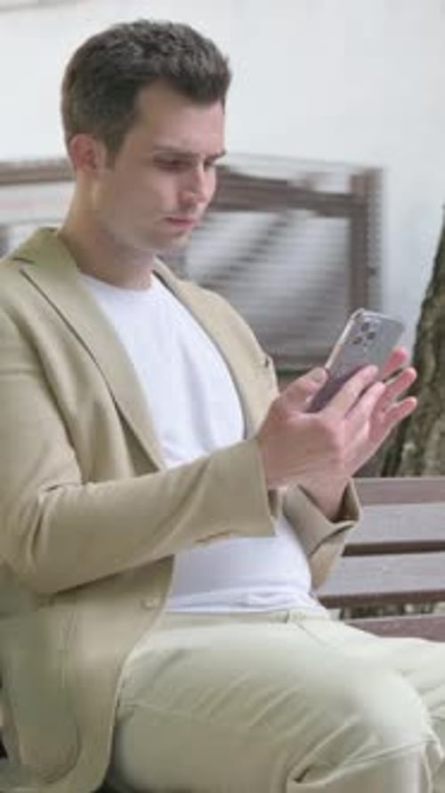 Man in Jacket Sitting and Using Mobile Phone