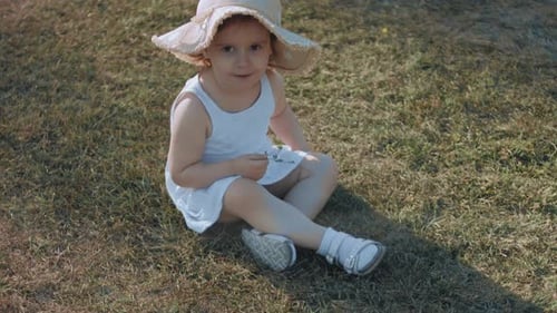 Happy Toddler Girl Wearing Sun Hat Sitting on the Green Grass on a Summer Day Summertime and Happy