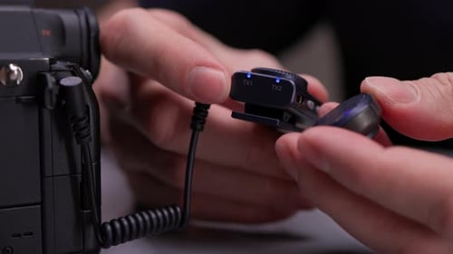 Closeup View of Videographer Hands Setting Up and Synchronizing Wireless Lapel Microphone System