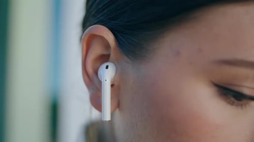 Woman Face With White Wireless Earbud In Ear Close Up. Portrait Of Young Trendy Girl Wearing Mode...