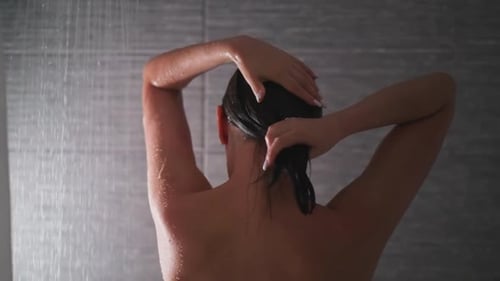 Frau wringt nasses Haar in der Duschkabine aus