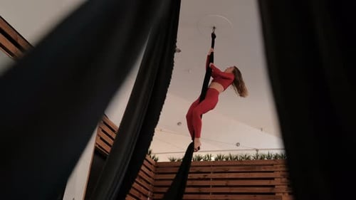 Young Woman in a Red Athletic Suit Does Complex Exercises on the Canvas Aerial Gymnastics in the