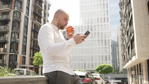 A Businessman on a Coffee Break is Texting on the Phone Near the Business Center
