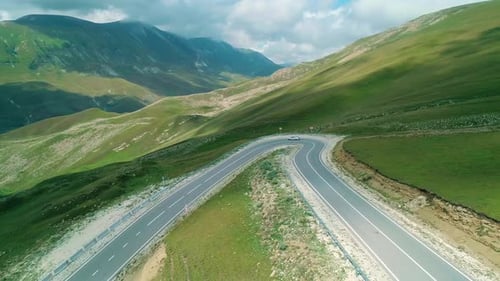 Aerial Over a Car Driving Along Winding Asphalt Road Among Mountains Covered with Green Grass in