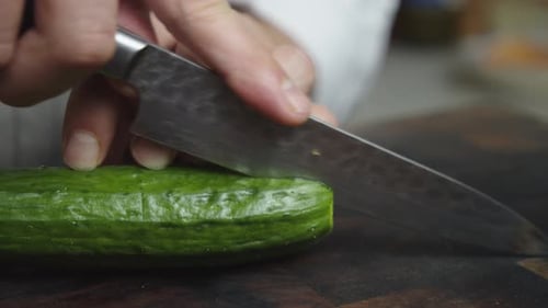 Cutting cucumber with kitchen knife in half. Close up on hands. Slow motion shot. Cooking healthy fo