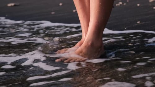 Women's Legs Without Hairline Stand on the Warm Sand of the Seashore