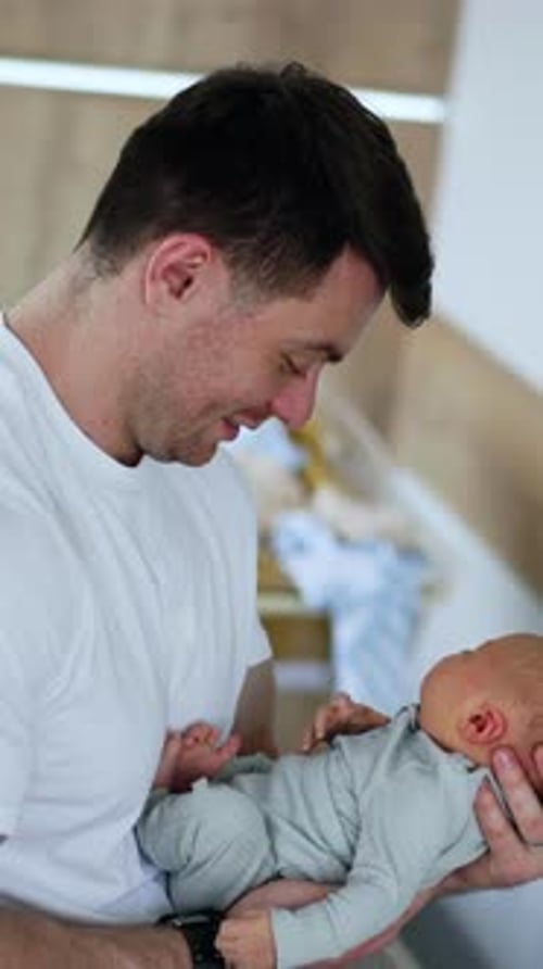 Happy new-made dad with a newborn in hands. Father waving his newborn in hospital ward.