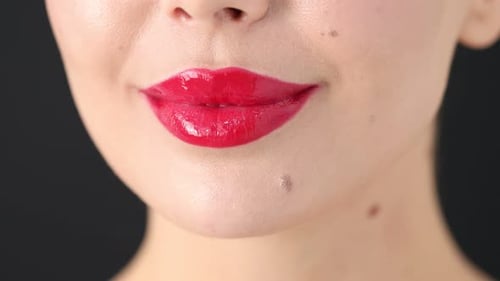Frau mit schönem roten Lippenstift auf ihren Lippen vor grauem Hintergrund, Makroansicht